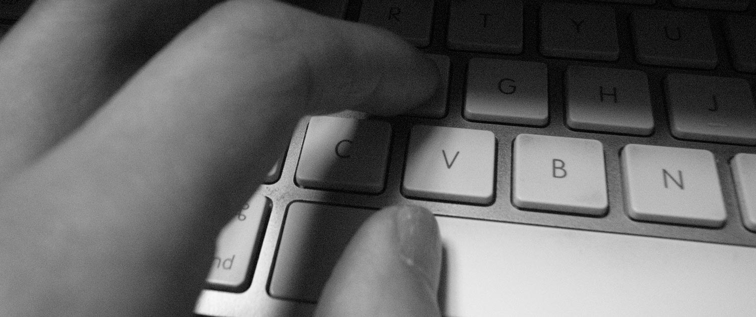 Photograph of a hand typing on an Apple keyboard